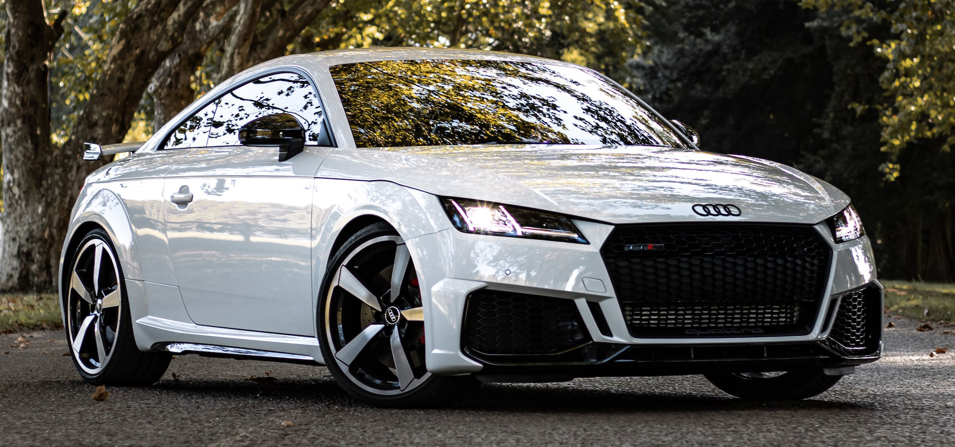 white audi car parked under trees with headlights on