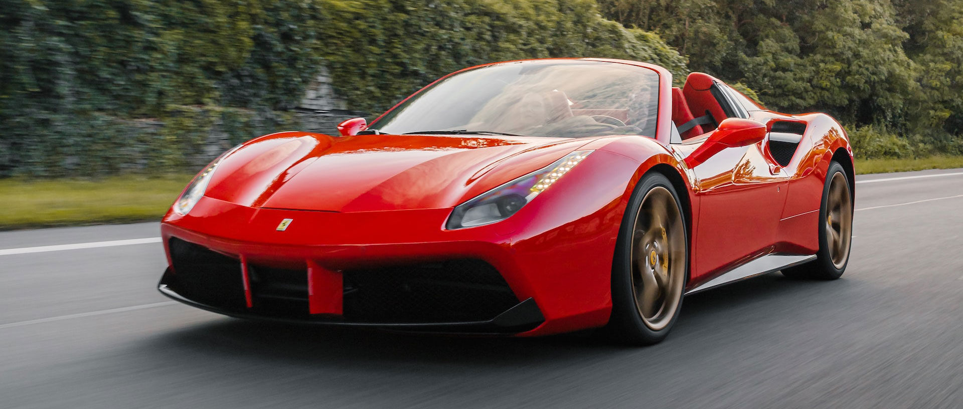 Red Ferrari driving down road with roof down